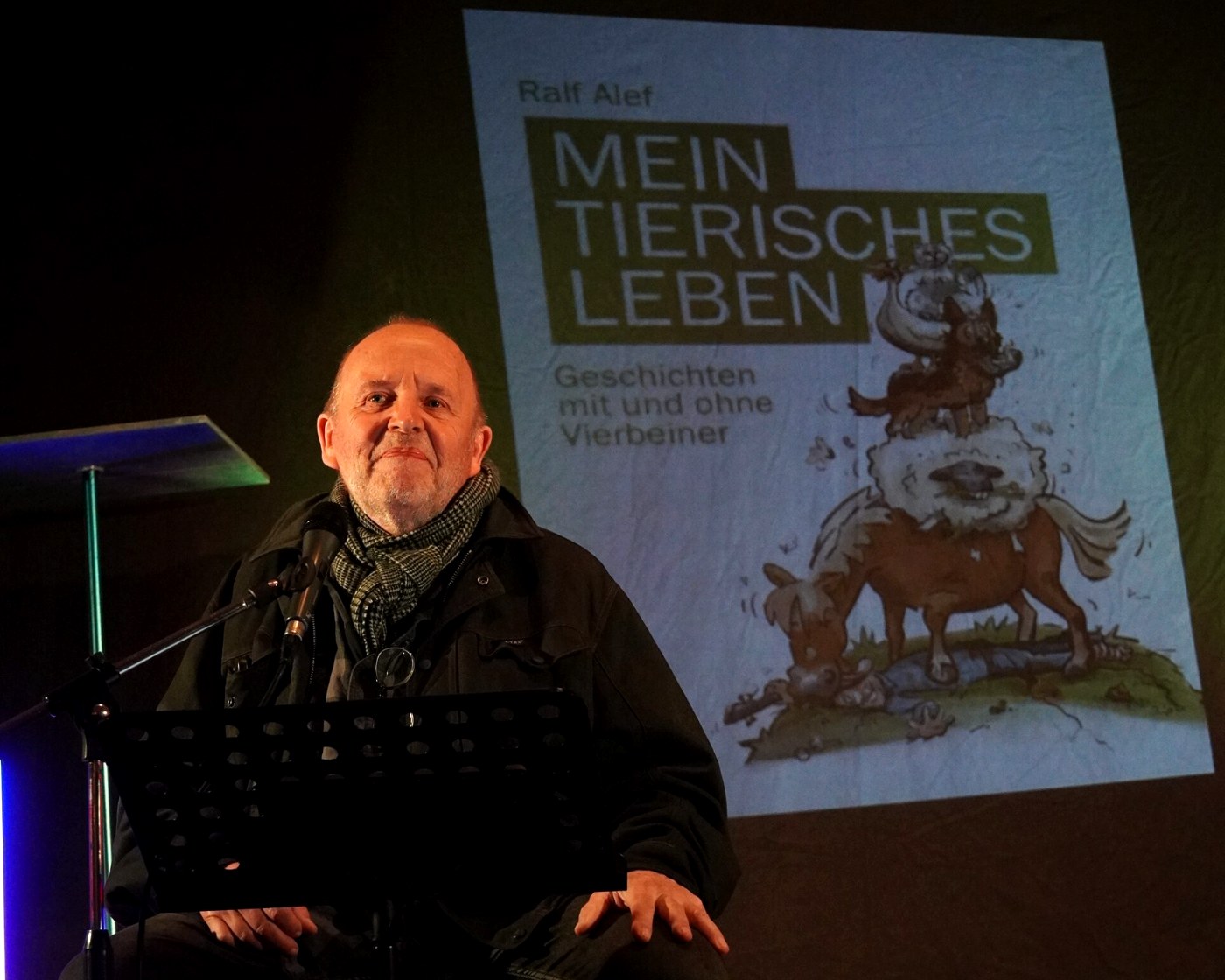 Ralf Alef bei einer Lesung, im Hintergrund das projizierte Buchcover Mein tierisches Leben